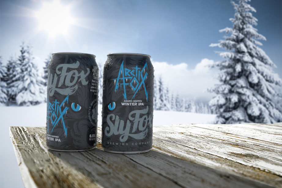 a can of a beer labeled "arctic fox" by Sly Fox Brewing company on a wooden table in the snow